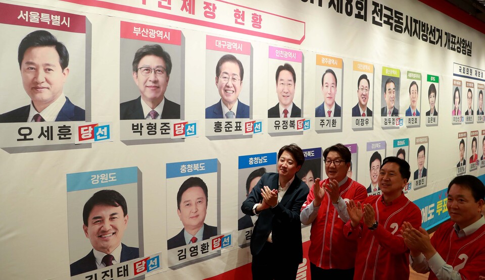 국민의힘 이준석 대표와 지도부가 1일 오후 국회 도서관 대강당에 마련된 지방선거 개표상황실에서 당선이 유력시되는 단체장 후보 사진 밑에 스티커를 붙인 뒤 박수치고 있다.  / 연합뉴스
