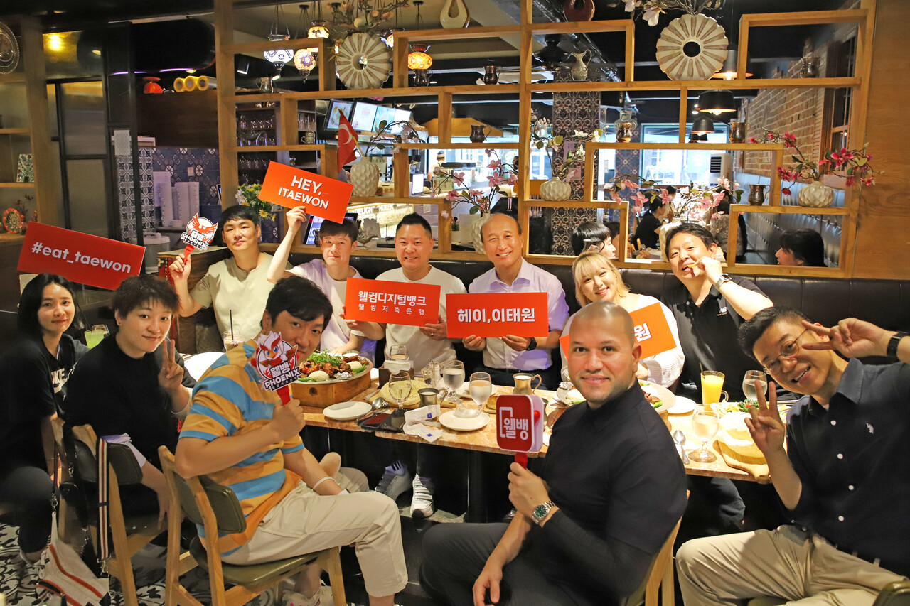 김대웅 웰컴저축은행 대표와 당행 프로당구팀 웰뱅피닉스 선수들이 이태원 상권 회복을 위한 ‘헤이 이태원 회식 챌린지’에 동참했다. (사진 왼쪽 앞줄부터) 웰뱅피닉스 최혜미 선수, 히가시우치 나츠미 선수, 웰컴저축은행 스포츠마케팅팀 구선모 과장, 비롤 위마즈 선수, 웰뱅피닉스 박성수 단장. (사진 왼쪽 뒷줄부터) 웰뱅피닉스 이상대 선수, 김임권 선수, 서현민 선수, 김대웅 웰뱅피닉스 구단주 겸 웰컴저축은행 대표이사, 김예은 선수, 웰컴저축은행 스포츠마케팅 장은석 팀장 /웰컴저축은행