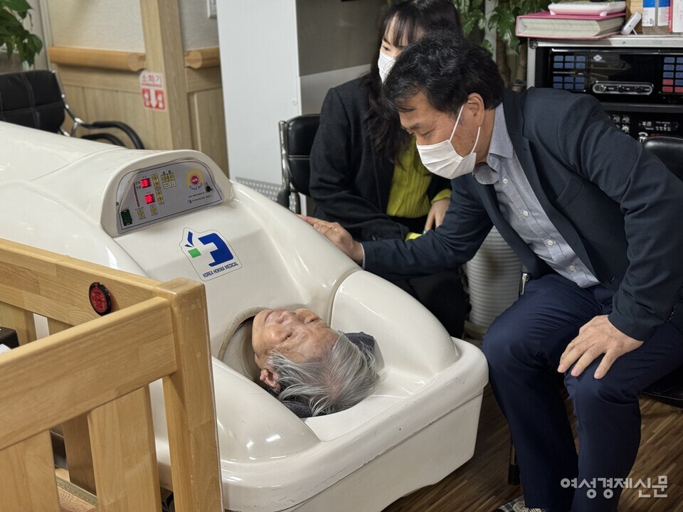 특별취재팀이 찜질기에 누워있는 82세 입소자와 대화하고 있다. /김현우 기자