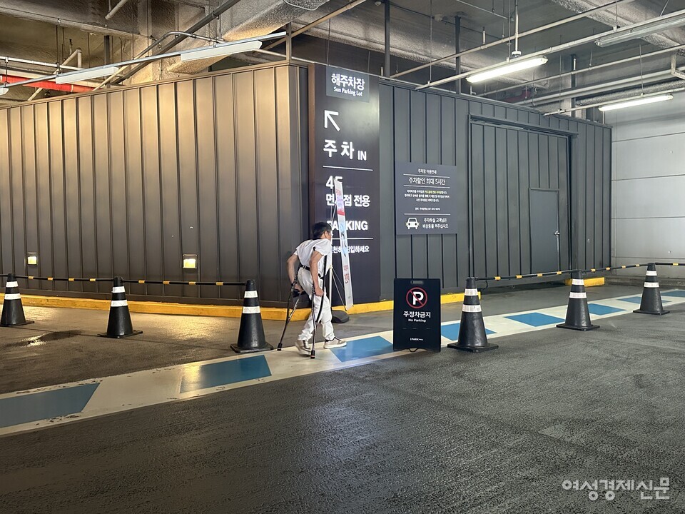 목발을 이용하는 이성수 씨가 용산 아이파크몰 장애인 전용 주차구역부터 출입구까지 보행 안전 통로를 통해 걸어가고 있다. 사진상 오른쪽은 차량이 들어오는 입구다. 보행 안전 통로와 차가 지나가는 경로가 겹칠 수밖에 없는 구조다. /여성경제신문