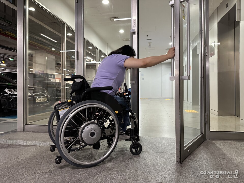 SK텔레콤 본사 지하 주차장과 연결되는 주 출입구 모습. 휠체어 이용자 홍서윤 씨(여·38)가 힘겹게 여닫이문을 열고 있다. /여성경제신문