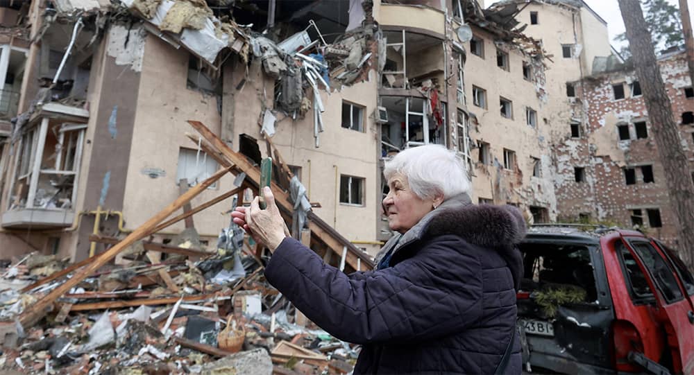 우크라이나 이르핀에서 최근 포격으로 파괴된 주거용 건물 앞에서 한 여성이 스마트폰을 사용해 사진을 올리고 있다. /로이터=연합뉴스